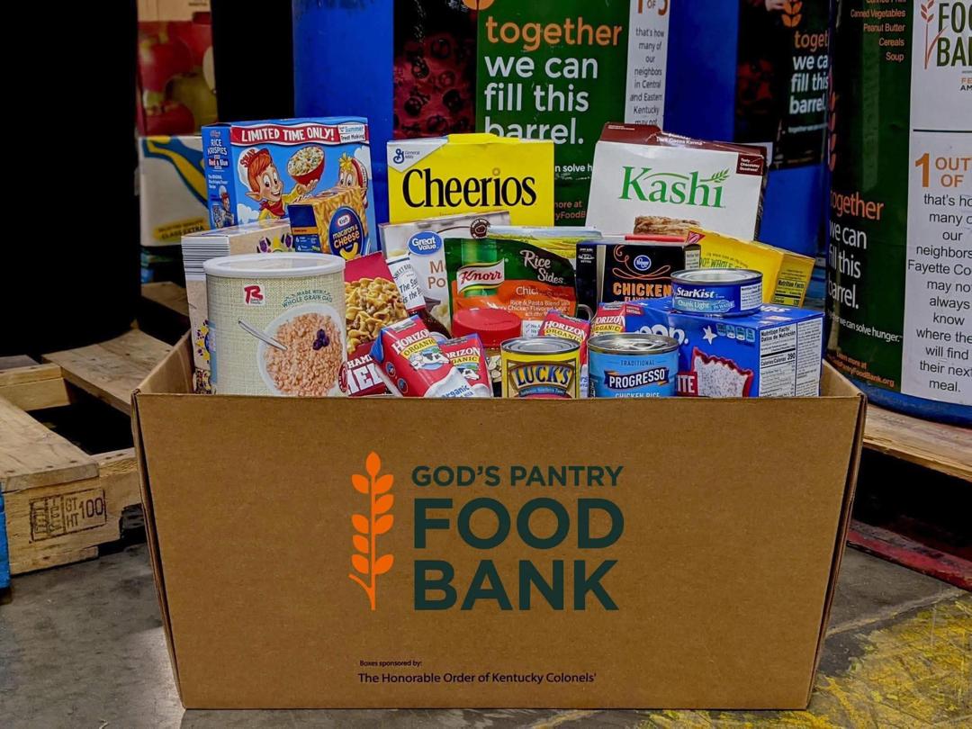 A cardboard box filled with grocery items including cereal, canned goods, and pantry staples